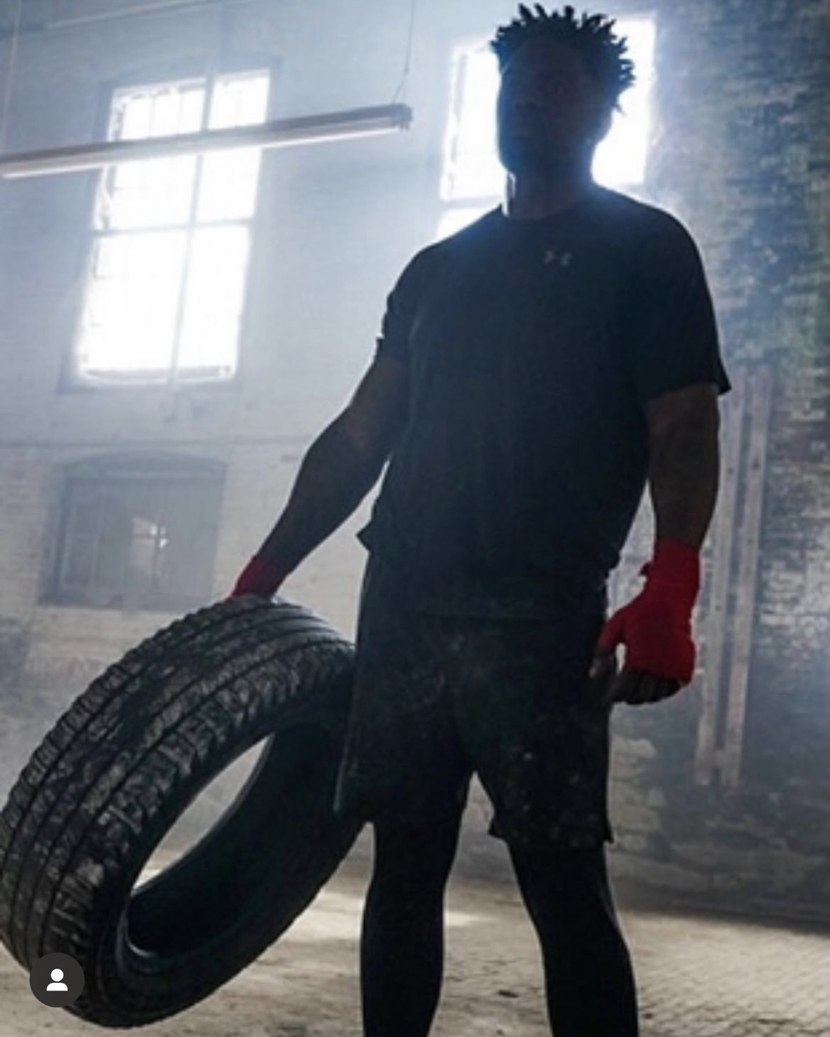 Athlete holding a tire in dim gym setting.